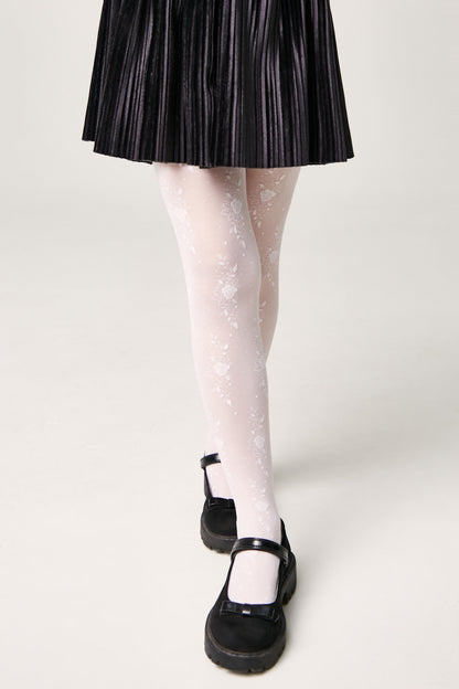 A pair of sheer white floral patterned tights worn with a black pleated skirt and black Mary Jane shoes against a white background.
