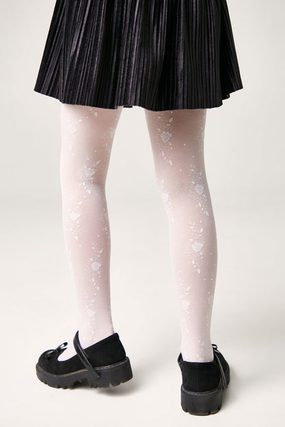 A person wears white floral-patterned tights underneath a black pleated skirt paired with black Mary Jane shoes.