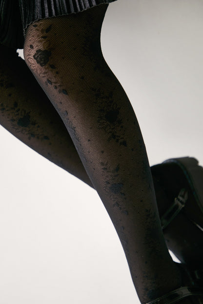 Black patterned tights featuring a delicate floral lace design worn with dark platform shoes against a plain white background.