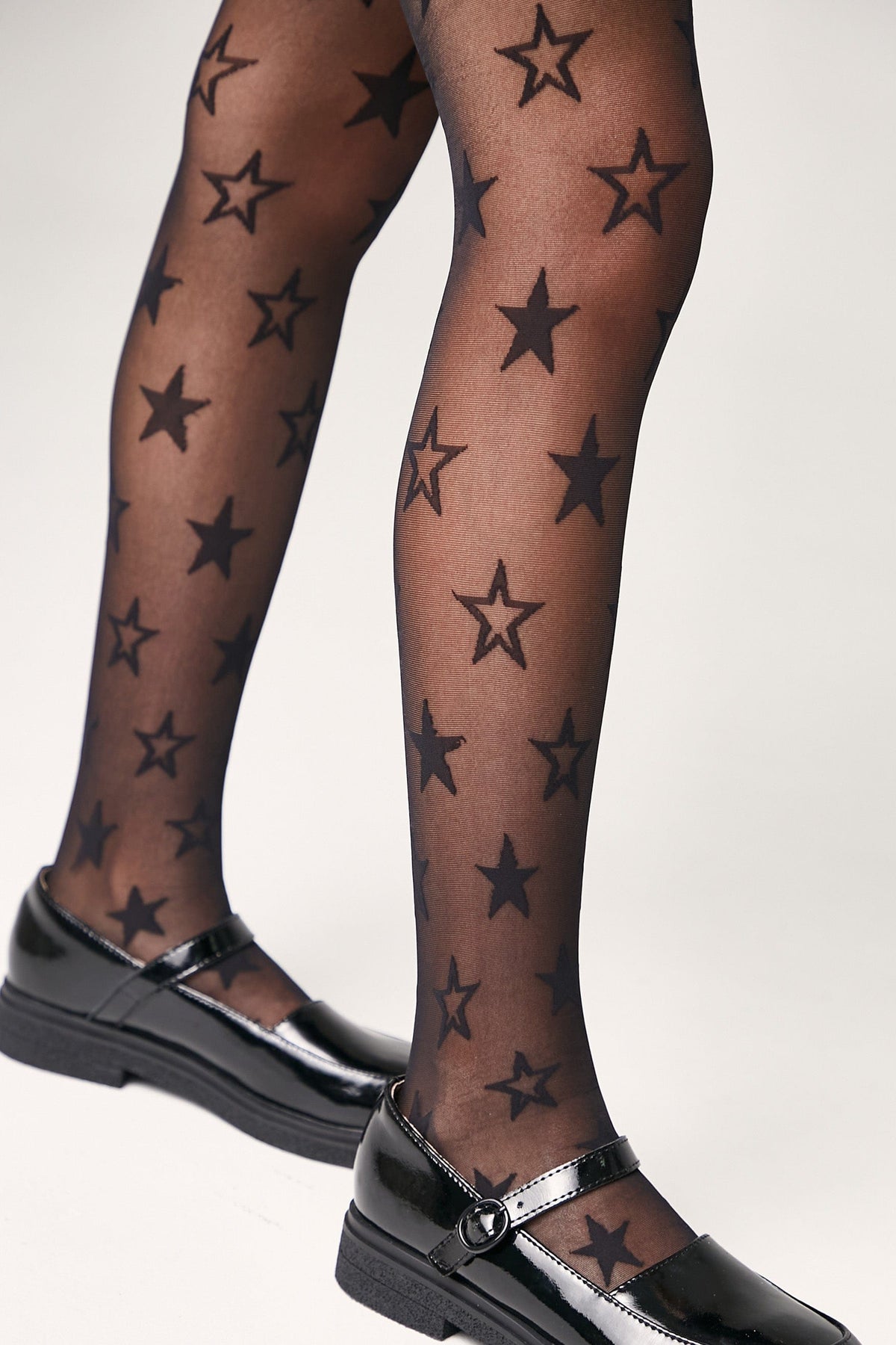 Black sheer tights patterned with various sizes of solid black stars, worn with black patent Mary Jane shoes.