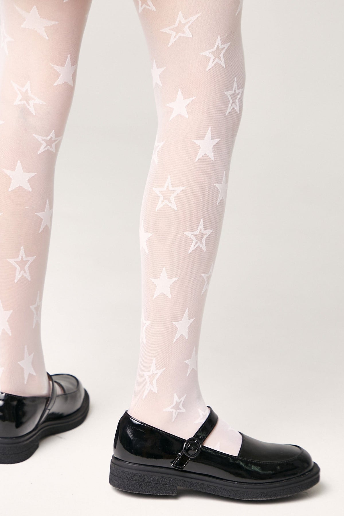 White tights featuring a recurring white star pattern worn with black patent leather Mary Jane shoes against a light grey background.