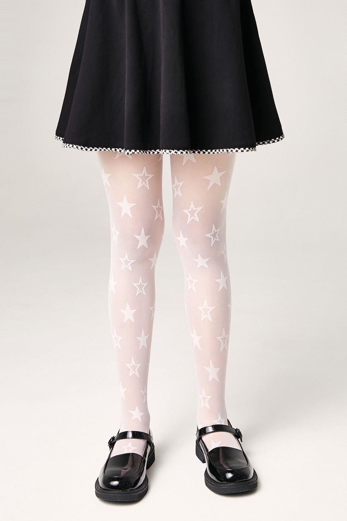 A person wears sheer white tights featuring a repeating pattern of five-pointed stars, paired with a black skirt and black Mary Jane shoes.