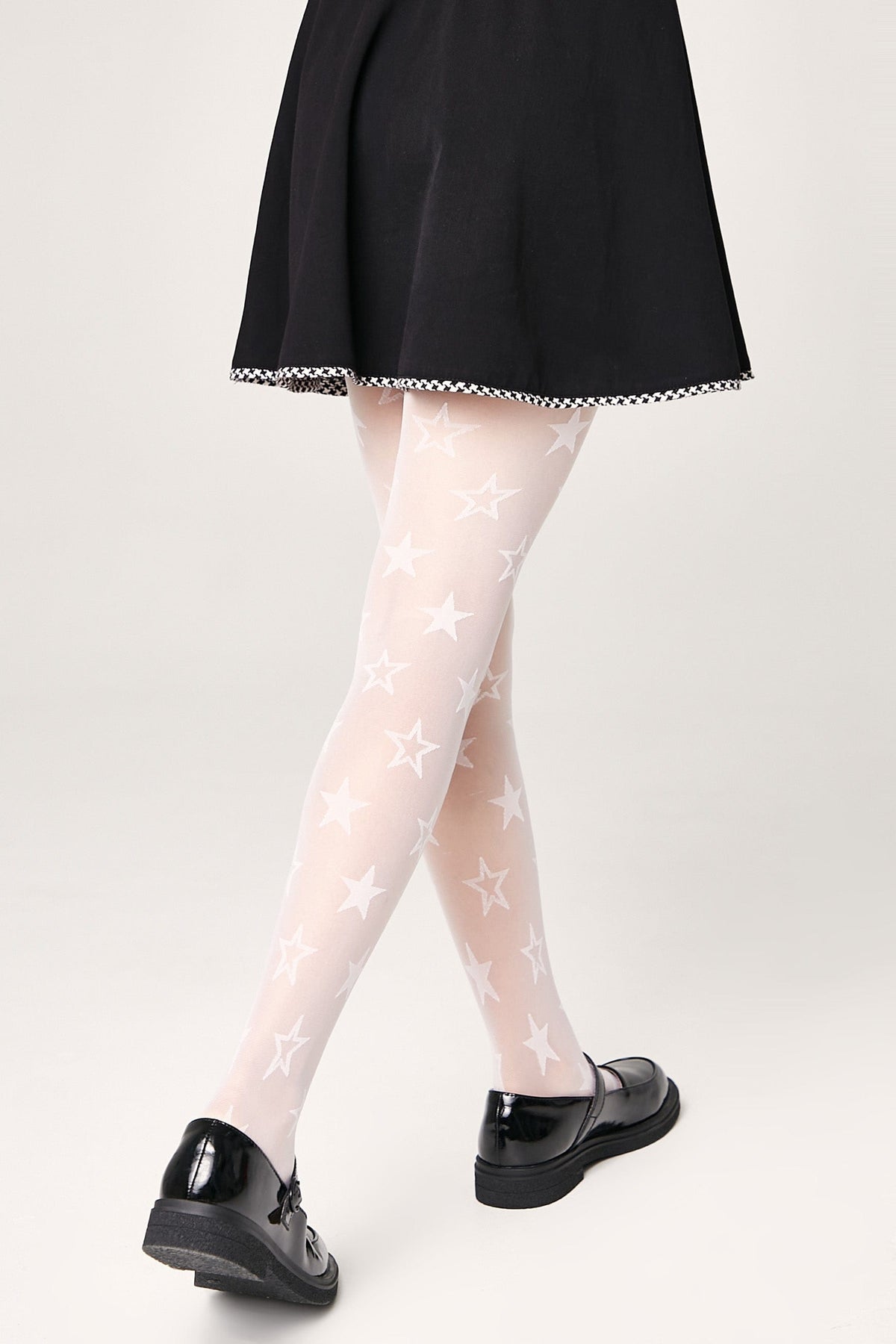 Sheer white tights featuring an all-over pattern of white stars, worn with a black skirt and black mary jane shoes.