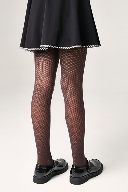Brown patterned tights with a textured honeycomb design are worn with a black skirt featuring a white houndstooth trim and black patent leather mary jane shoes.
