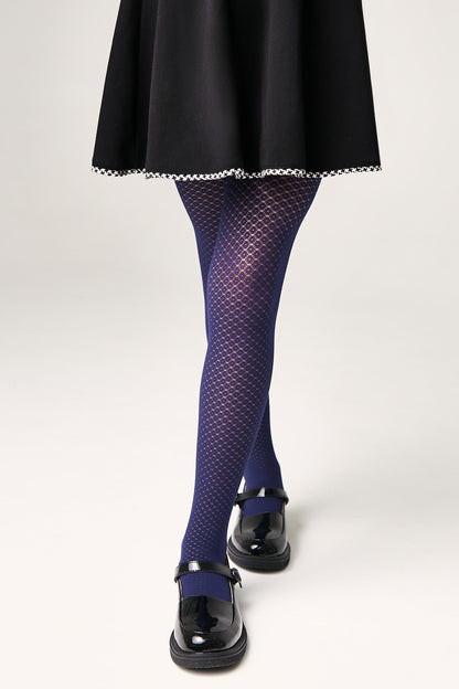 A person wears navy blue textured tights with a subtle diamond pattern, paired with a black skirt with white trim and black patent leather Mary Jane shoes against a plain white background.