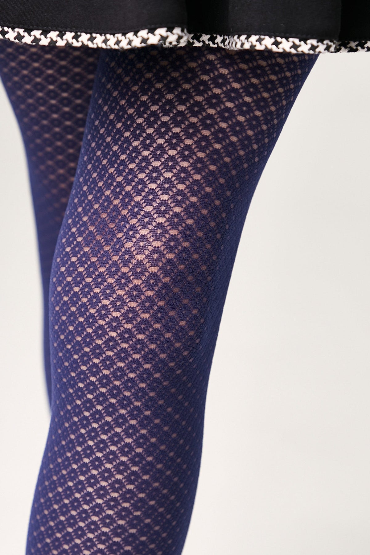 Navy blue patterned tights featuring a repeating diamond-shaped mesh design, worn under a black skirt with a white patterned hem.