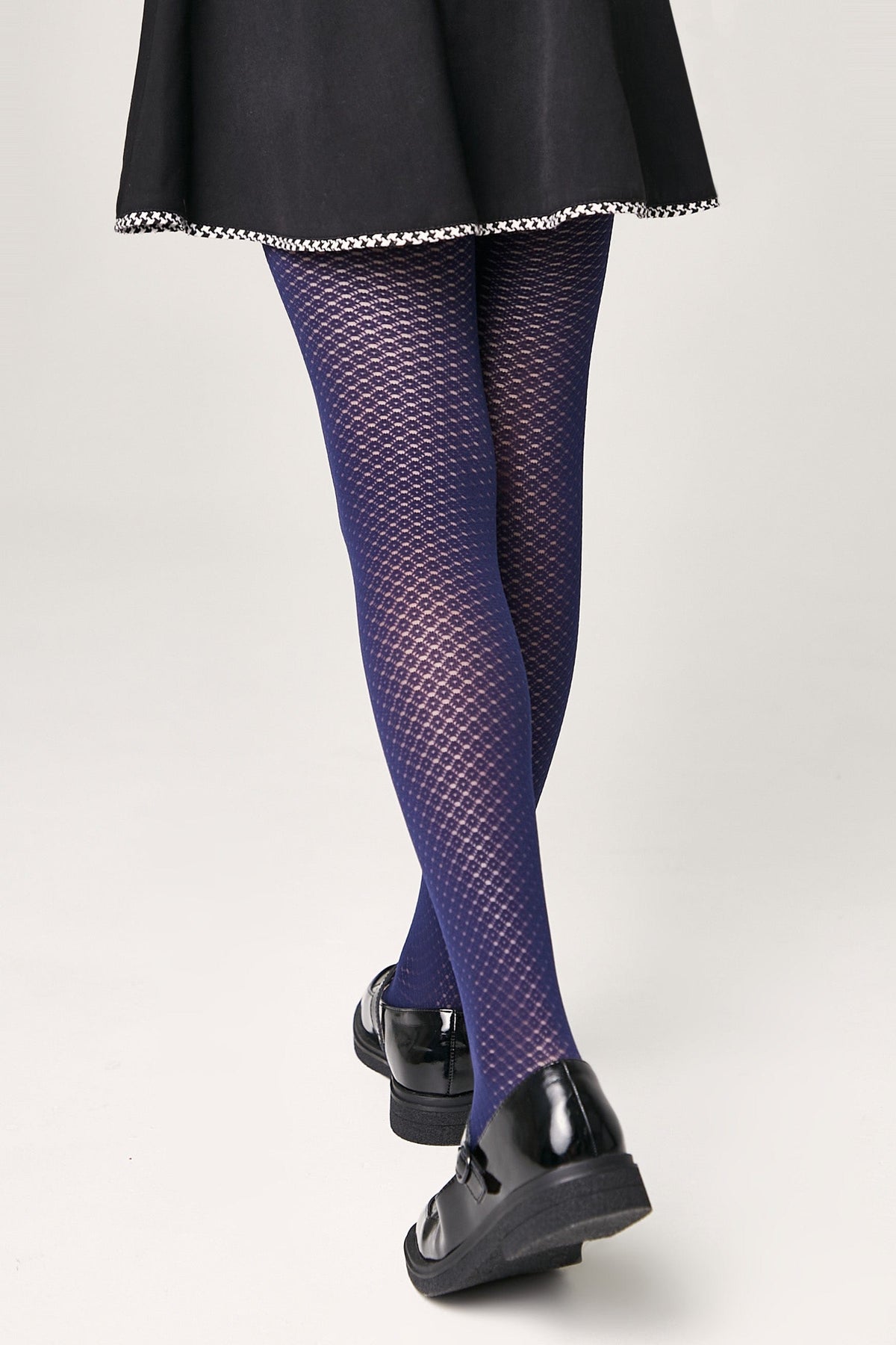 Blue textured tights with a geometric pattern are worn with a black skirt and black shiny shoes.