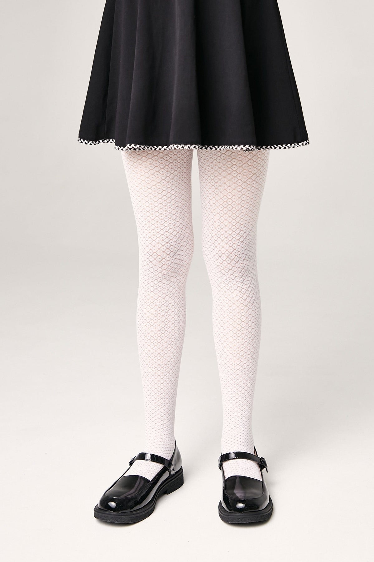 A person wears white patterned tights, a black skirt with a checkered hem, and black Mary Jane shoes against a plain background.
