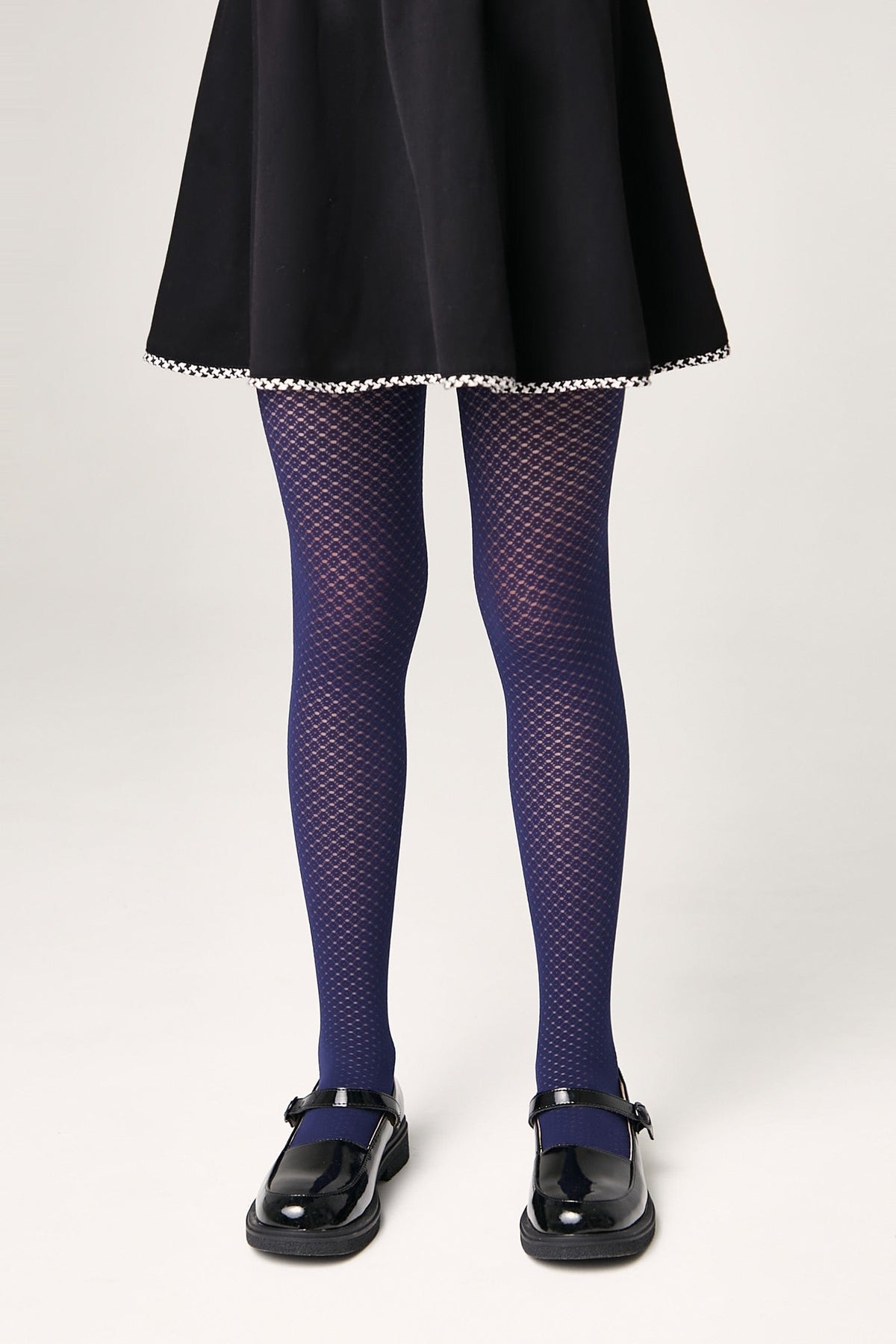 A person wears navy blue textured patterned tights with a black skirt and black shiny Mary Jane shoes.