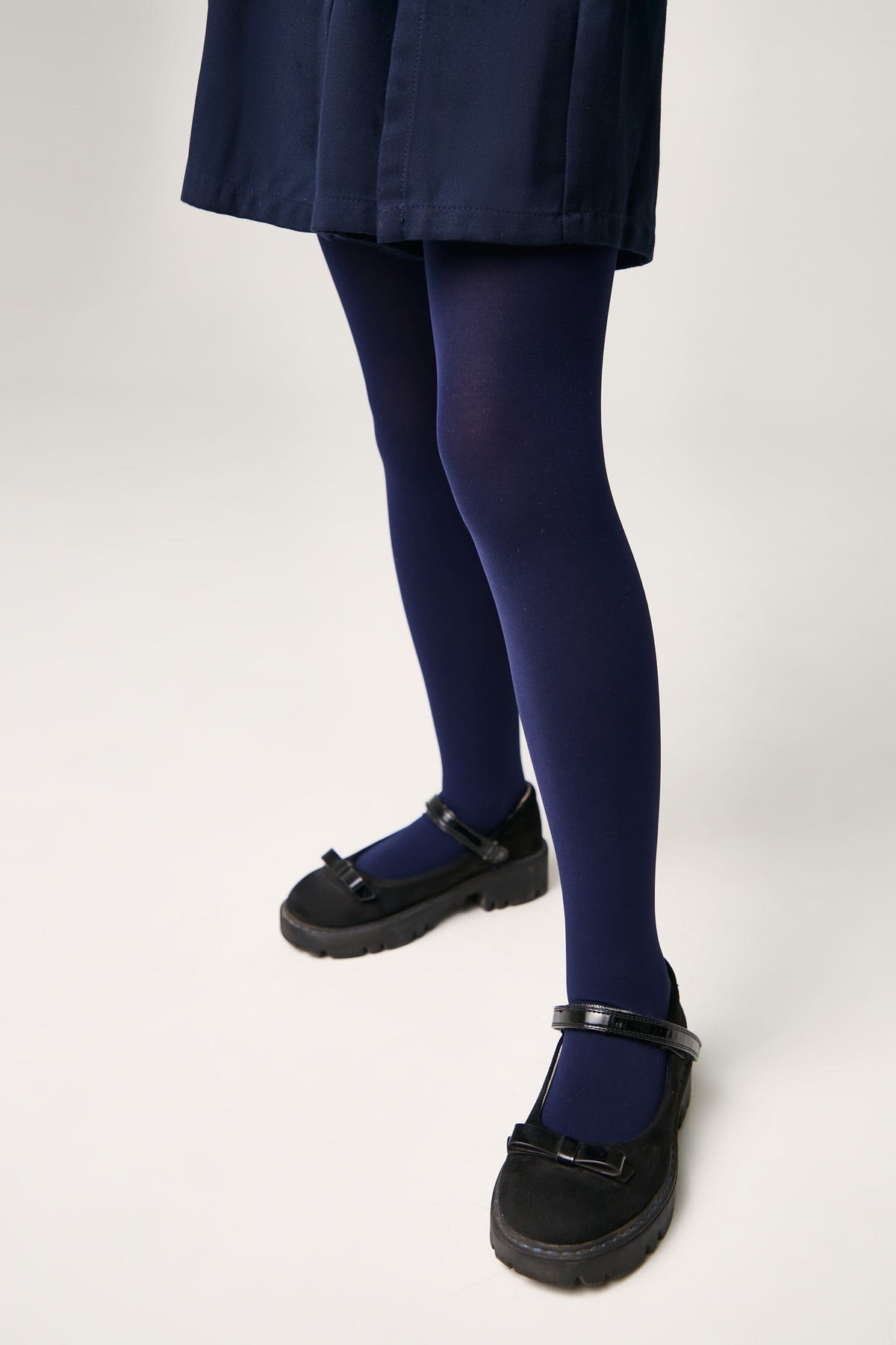 A pair of opaque navy blue tights worn with black Mary Jane style shoes featuring thick lug soles and a small bow detail on the strap.