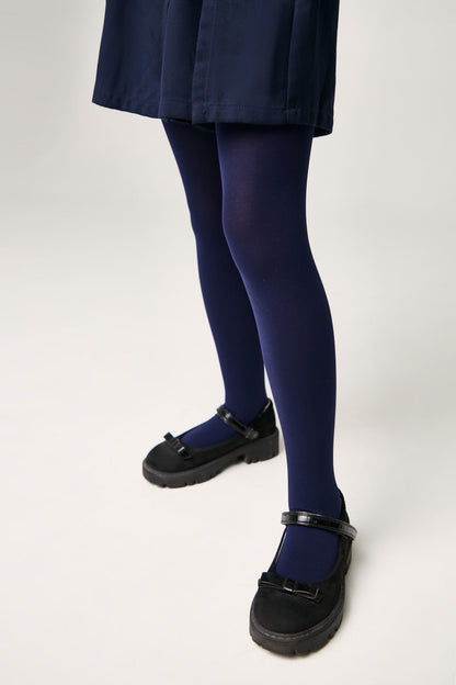 A pair of opaque navy blue tights worn with black Mary Jane style shoes featuring thick lug soles and a small bow detail on the strap.
