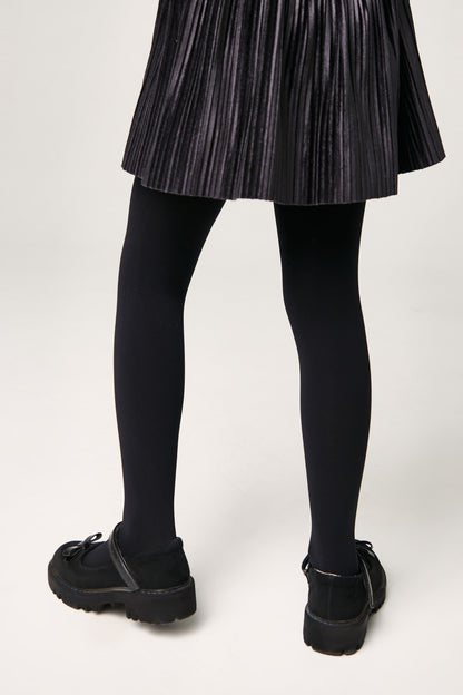 A person wears a pleated black skirt, opaque black tights, and black Mary Jane shoes with thick lug soles.