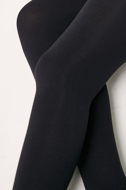 A close-up view of legs wearing opaque black tights against a plain white background.