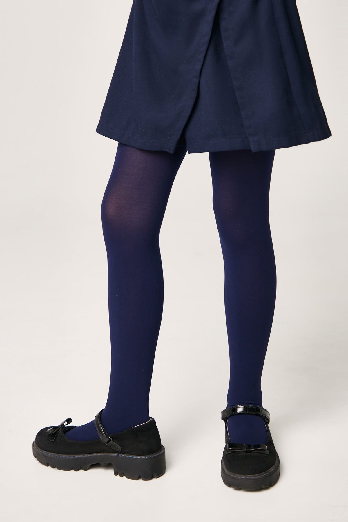 A pair of opaque navy blue tights worn with a navy blue skirt and black patent leather Mary Jane shoes with thick lug soles.