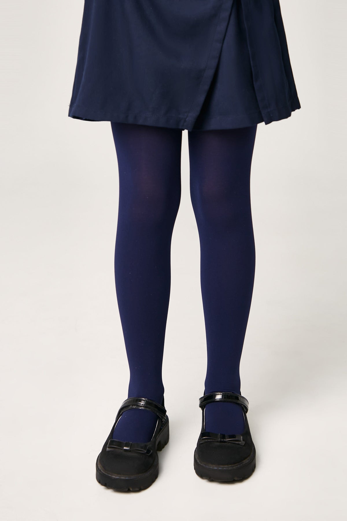 A pair of opaque navy blue tights worn with a navy blue skirt and black Mary Jane shoes.