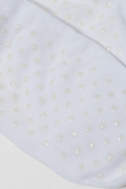 A close-up view of white socks featuring a repeating pattern of small, translucent, circular grip dots on the fabric surface.