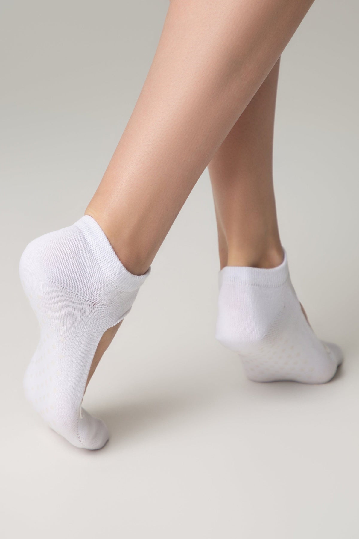 A pair of white ankle socks worn on the feet of a person standing against a plain light gray background.