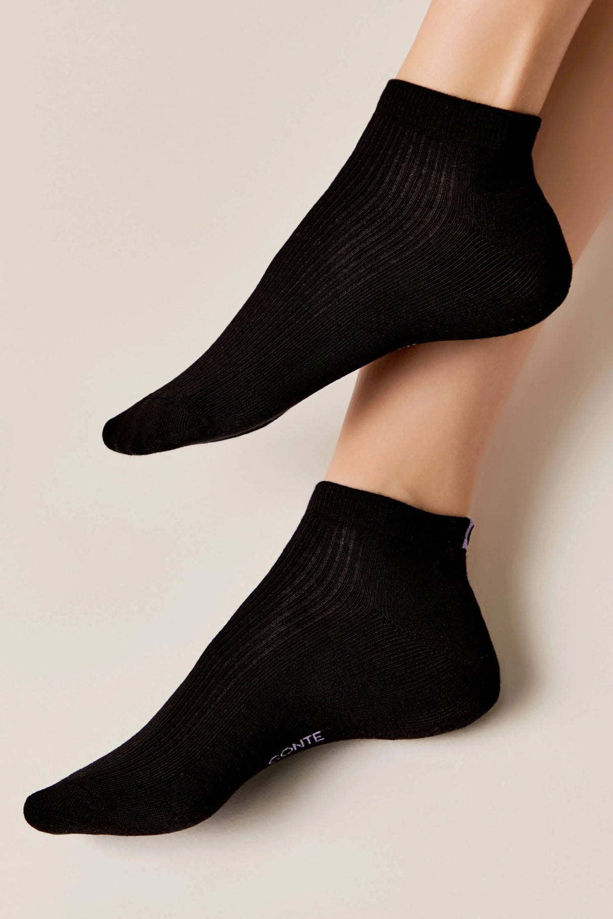 A pair of black ribbed ankle socks worn on feet against a plain beige background.