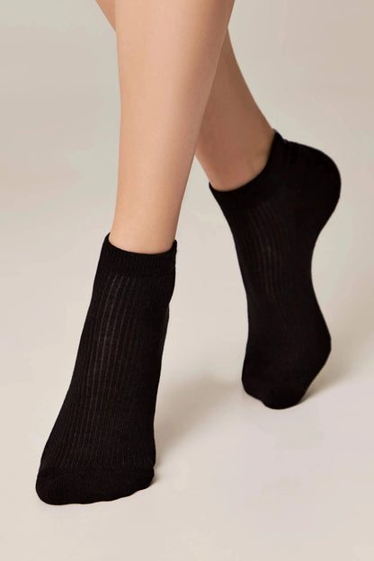 A person wearing plain black ribbed ankle socks against a solid light background.