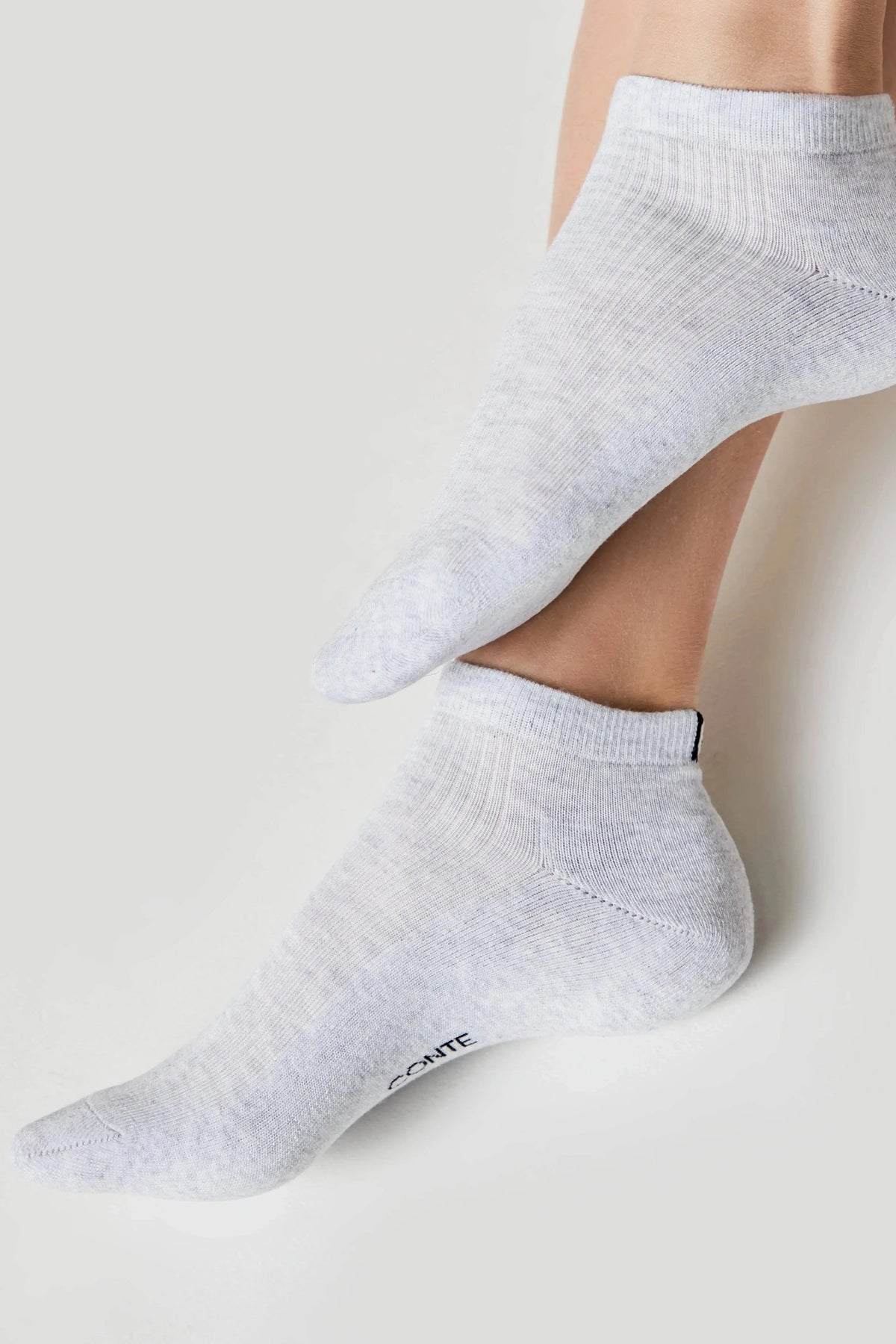 Light grey low-cut ankle socks on a person's feet against a white background.