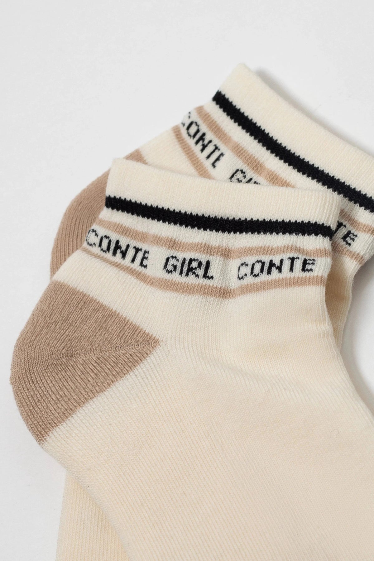 Ankle socks in a light cream color feature a beige heel, a beige horizontal stripe across the cuff, and a thin black band with the repeating black text "CONTE GIRL" printed on the top cuff.