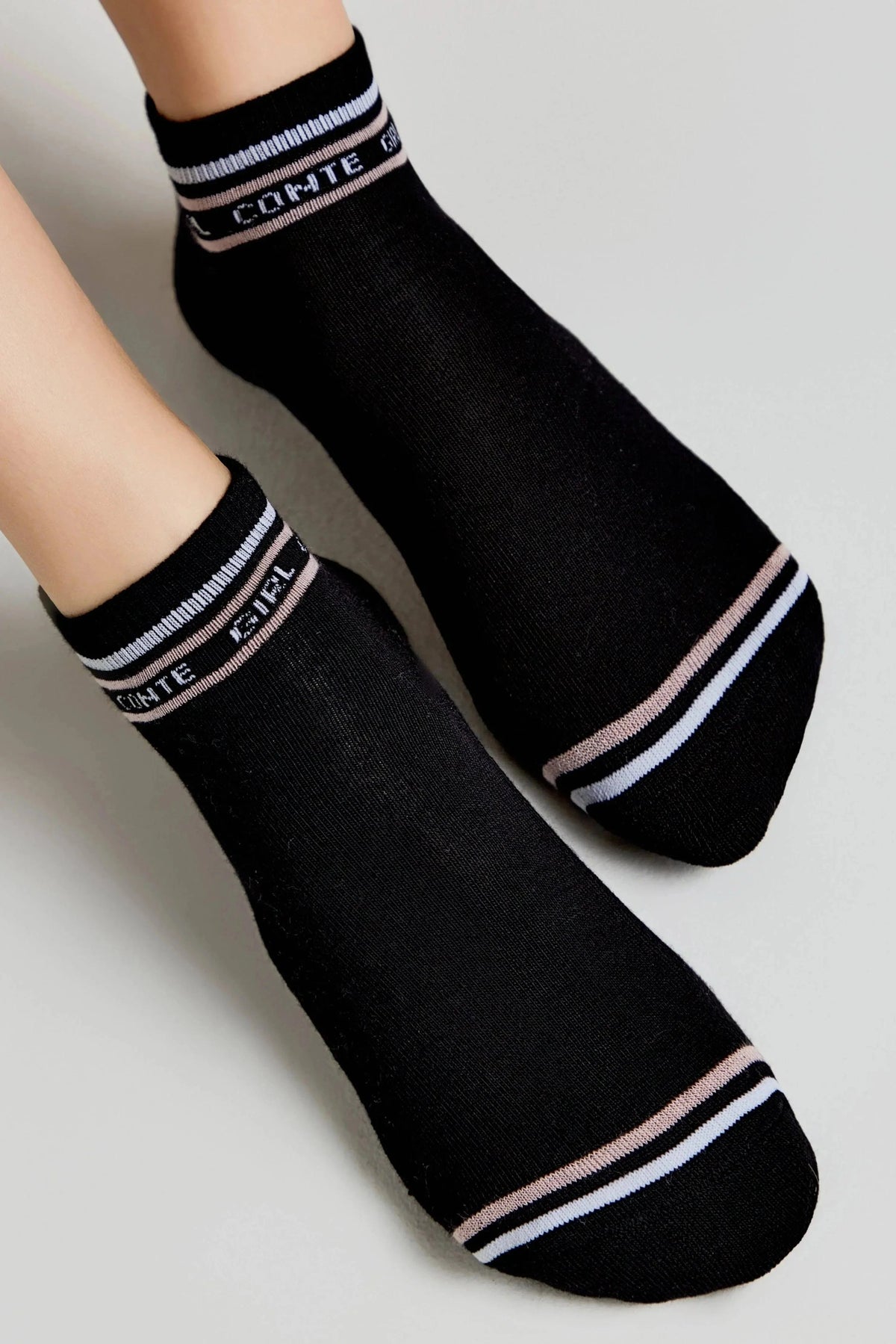 A pair of black ankle socks featuring a white and light pink striped cuff with white text and matching stripes near the toe.