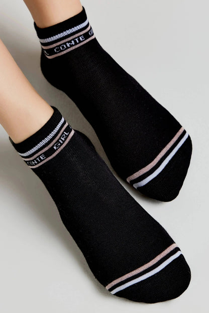 A pair of black ankle socks featuring a white and light pink striped cuff with white text and matching stripes near the toe.