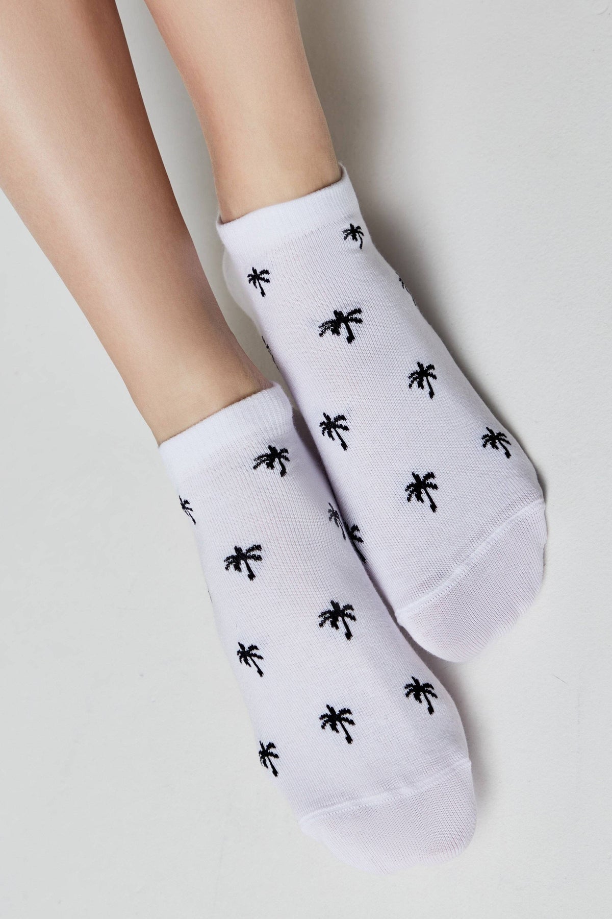 A pair of white ankle socks patterned with small black palm tree icons worn on a person's feet.