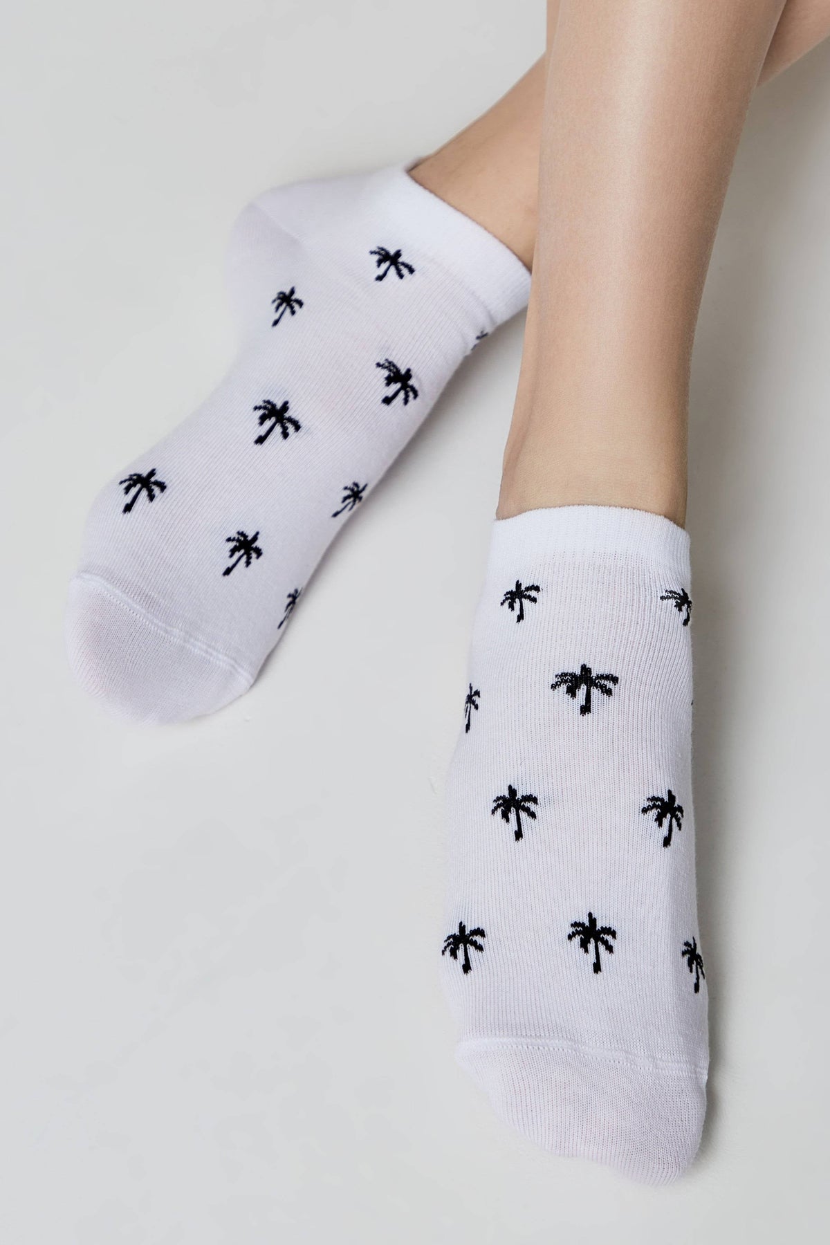 A pair of white ankle socks patterned with small black palm trees worn on a person's feet.