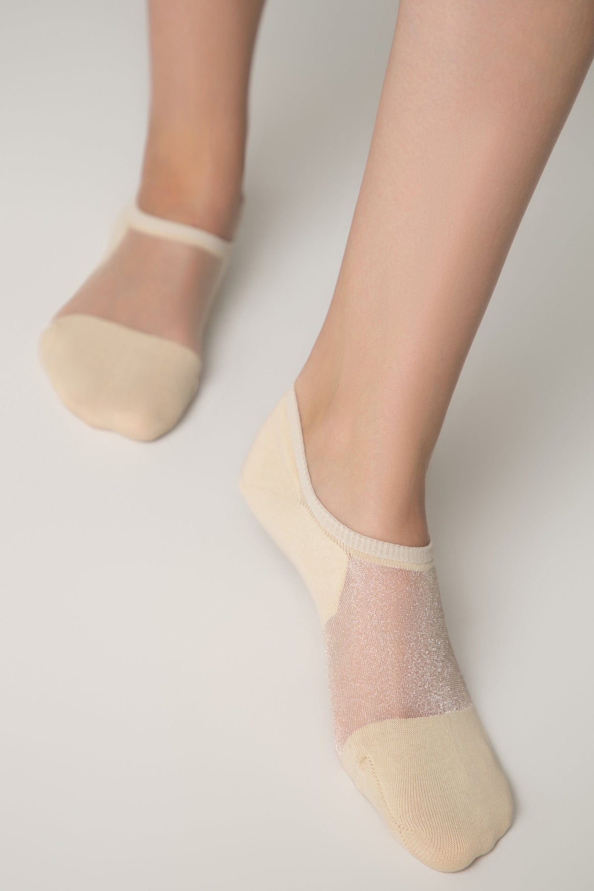 A pair of beige low-cut no-show socks worn on a person's feet, featuring a sheer shimmering panel across the top of the foot and a solid-colored toe and heel section.