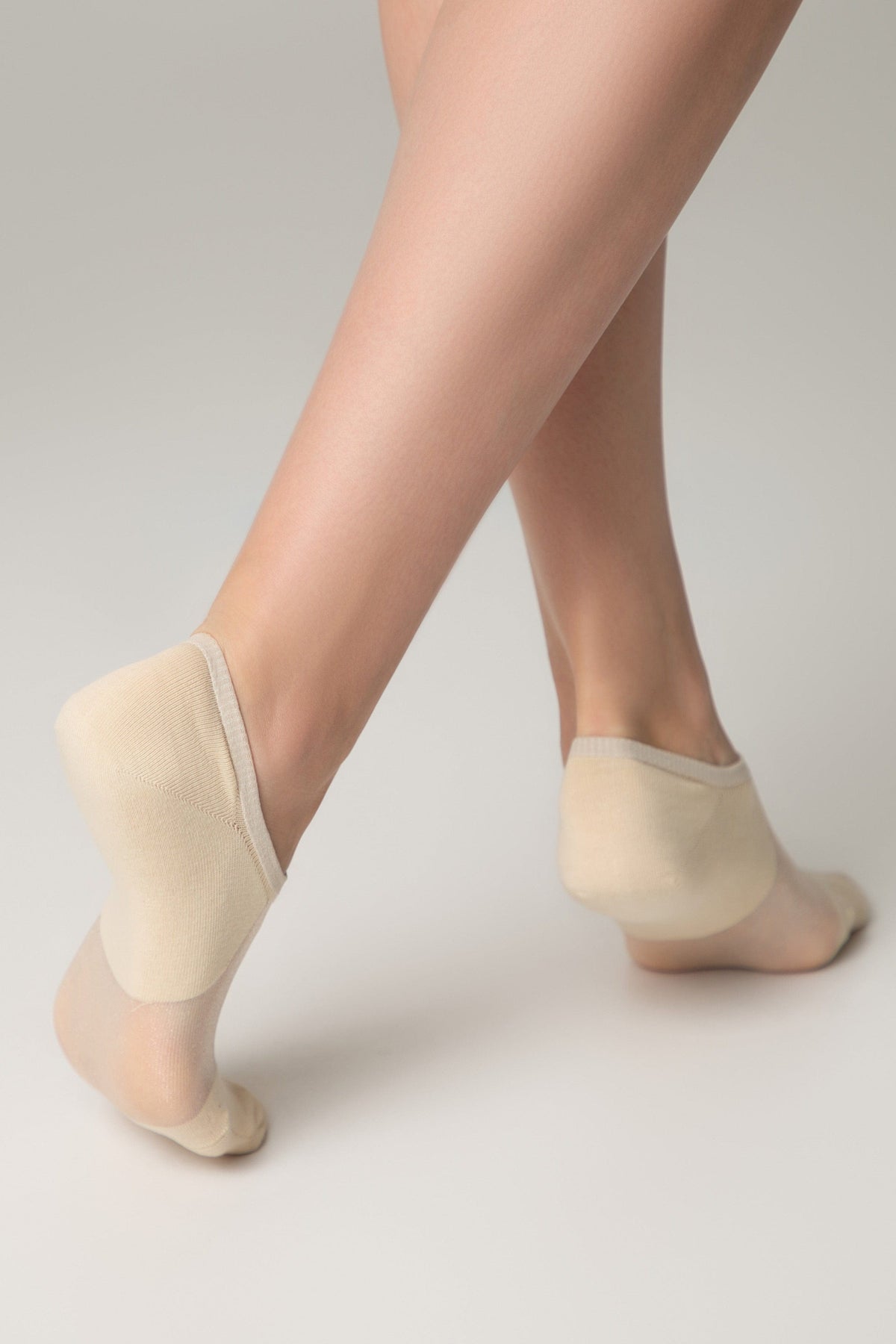 Beige no-show socks worn on feet posed on a plain light grey background.