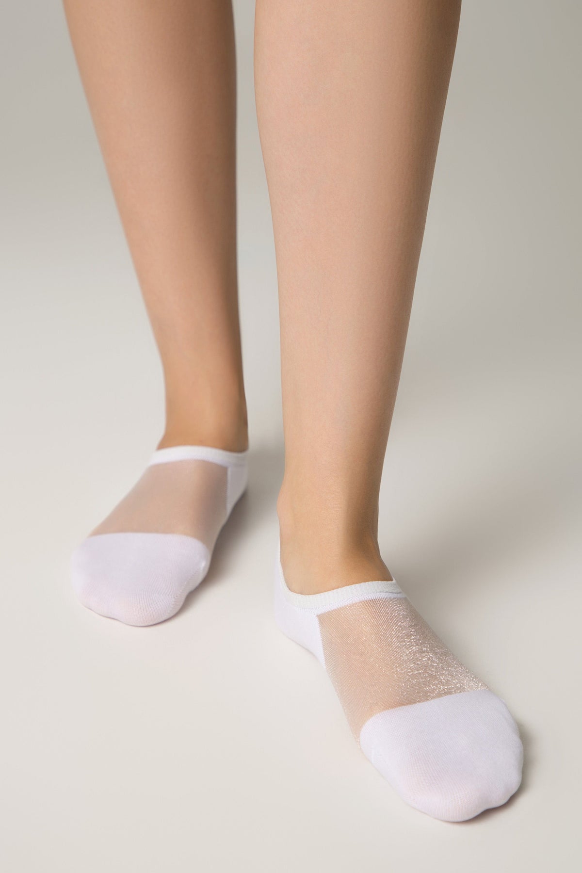 A pair of white low-cut ankle socks with a sheer, shimmering mesh top panel worn on a person's feet against a plain light background.