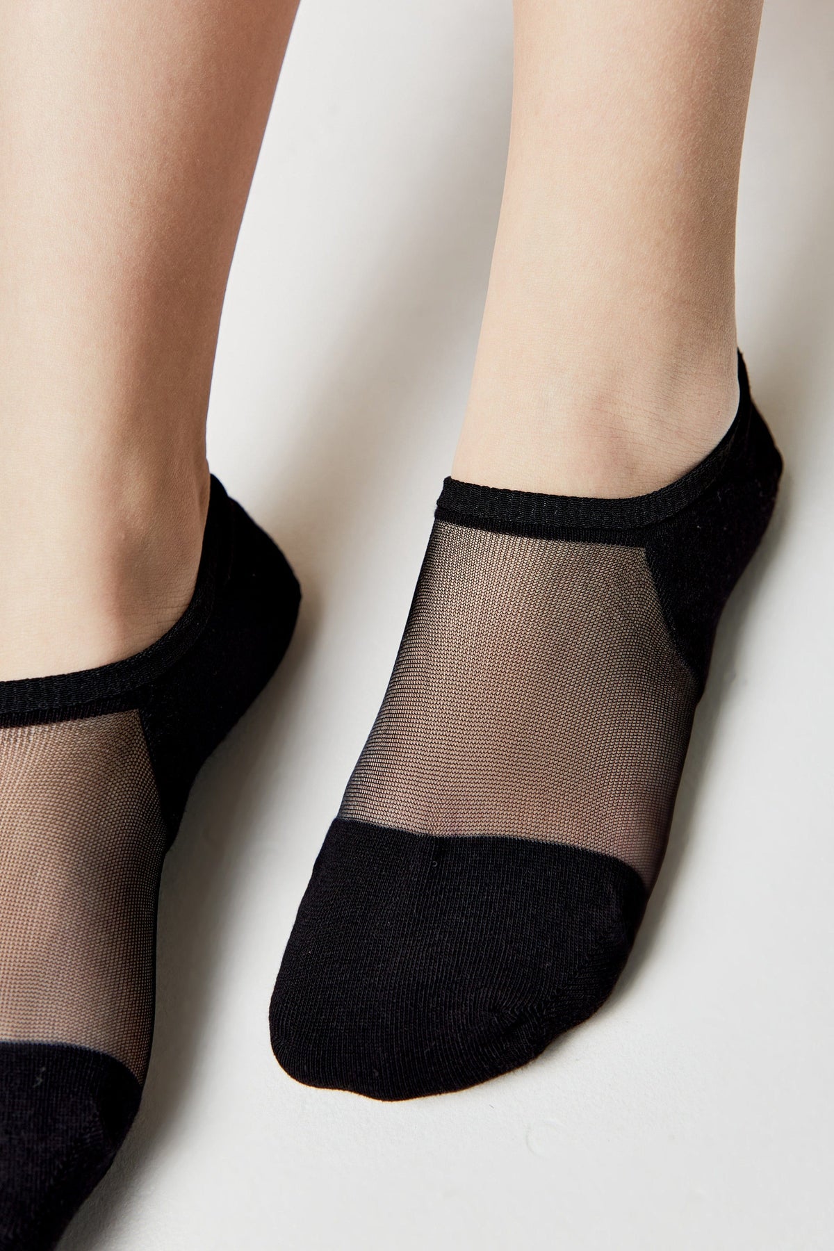 A pair of black no-show socks with a sheer mesh top panel worn on a person's feet against a plain light background.