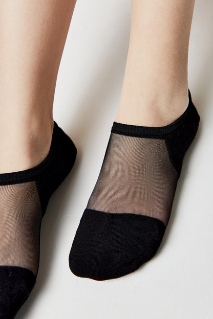A pair of black no-show socks with a sheer mesh top panel worn on a person's feet against a plain light background.