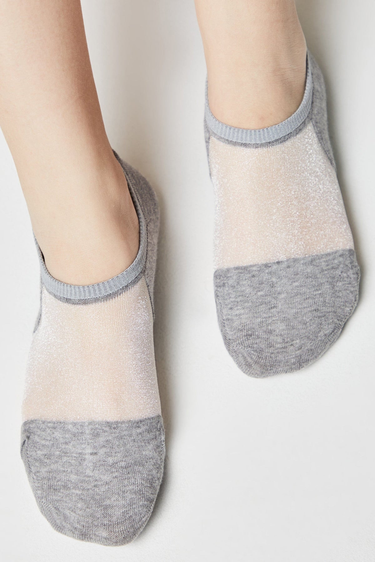 A pair of grey low-cut socks with a sheer, sparkling mesh panel across the top of the foot worn on a person's feet against a plain white background.
