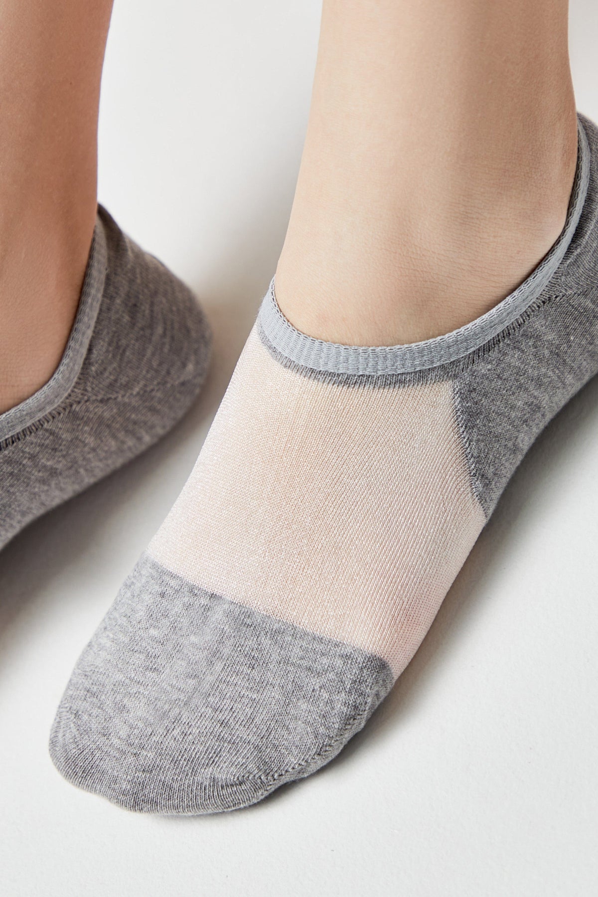 A pair of low-cut, ankle socks feature a color-blocked design with gray knit fabric at the heel and toe, transitioning into a sheer, pale pink mesh panel across the top of the foot.