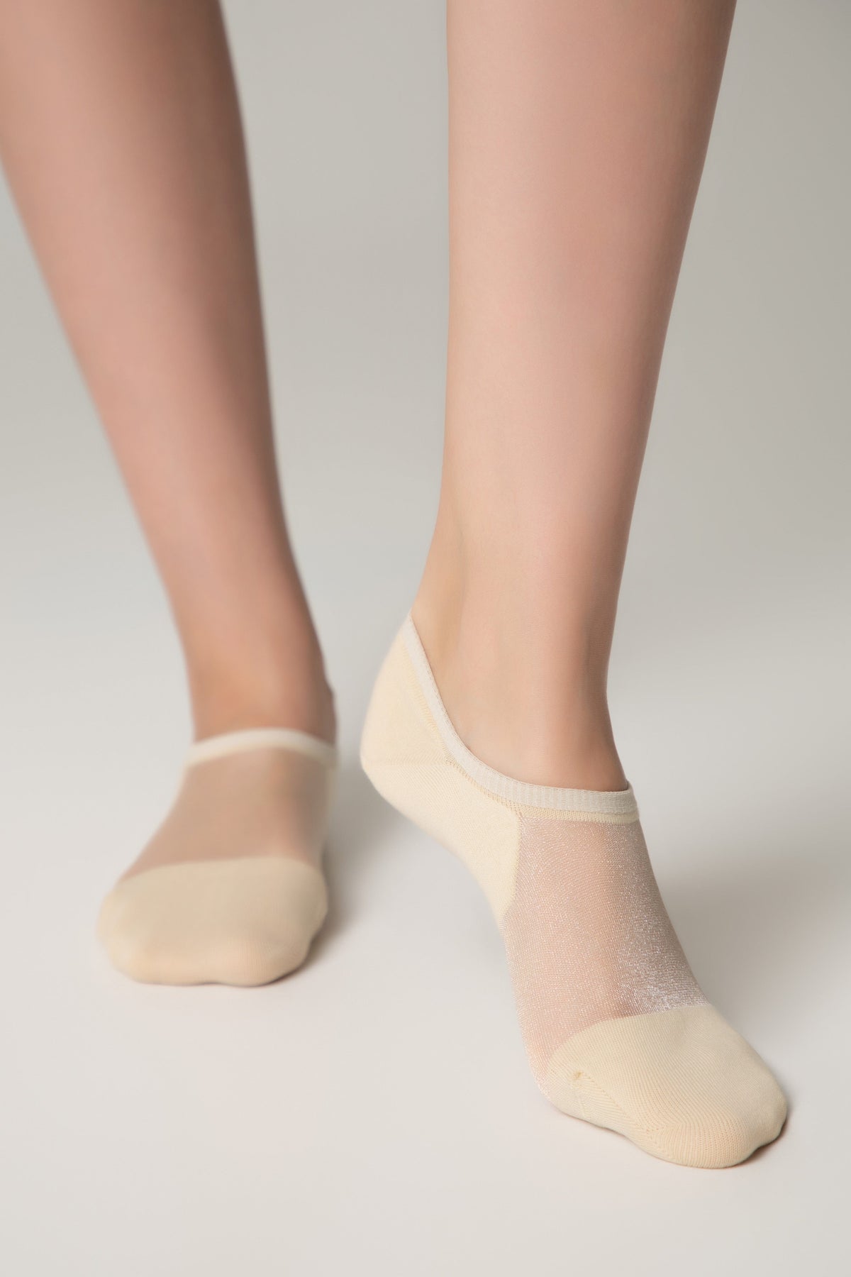 Beige no-show socks with a sheer, shimmering mesh top and solid fabric toe and heel sections worn on a pair of legs against a plain white background.