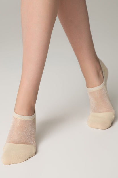 Beige no-show socks with a sheer, shimmering knit fabric on the instep, worn on a person's feet against a plain light background.