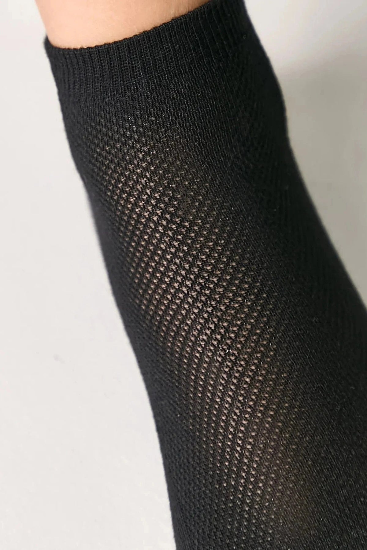 A close-up view of a black knit sock with a distinct, textured diamond-shaped mesh pattern.