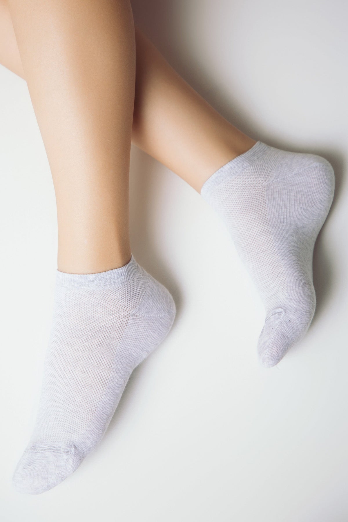 A pair of light gray ankle socks worn on feet against a clean white background.