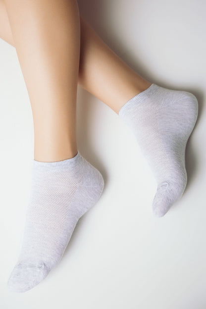 A pair of light gray ankle socks worn on feet against a clean white background.