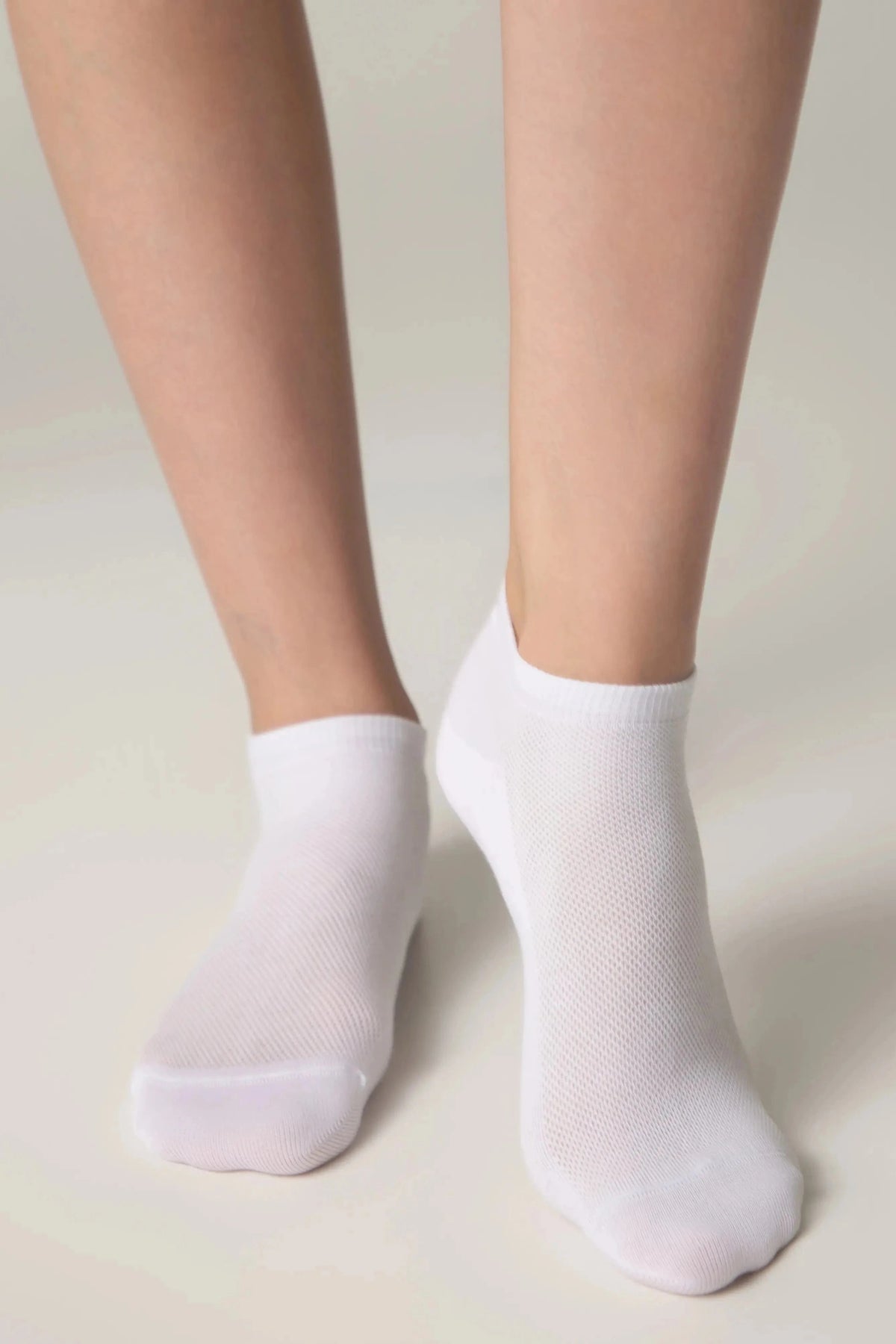 A pair of white ankle socks worn on a person's feet against a plain light background.