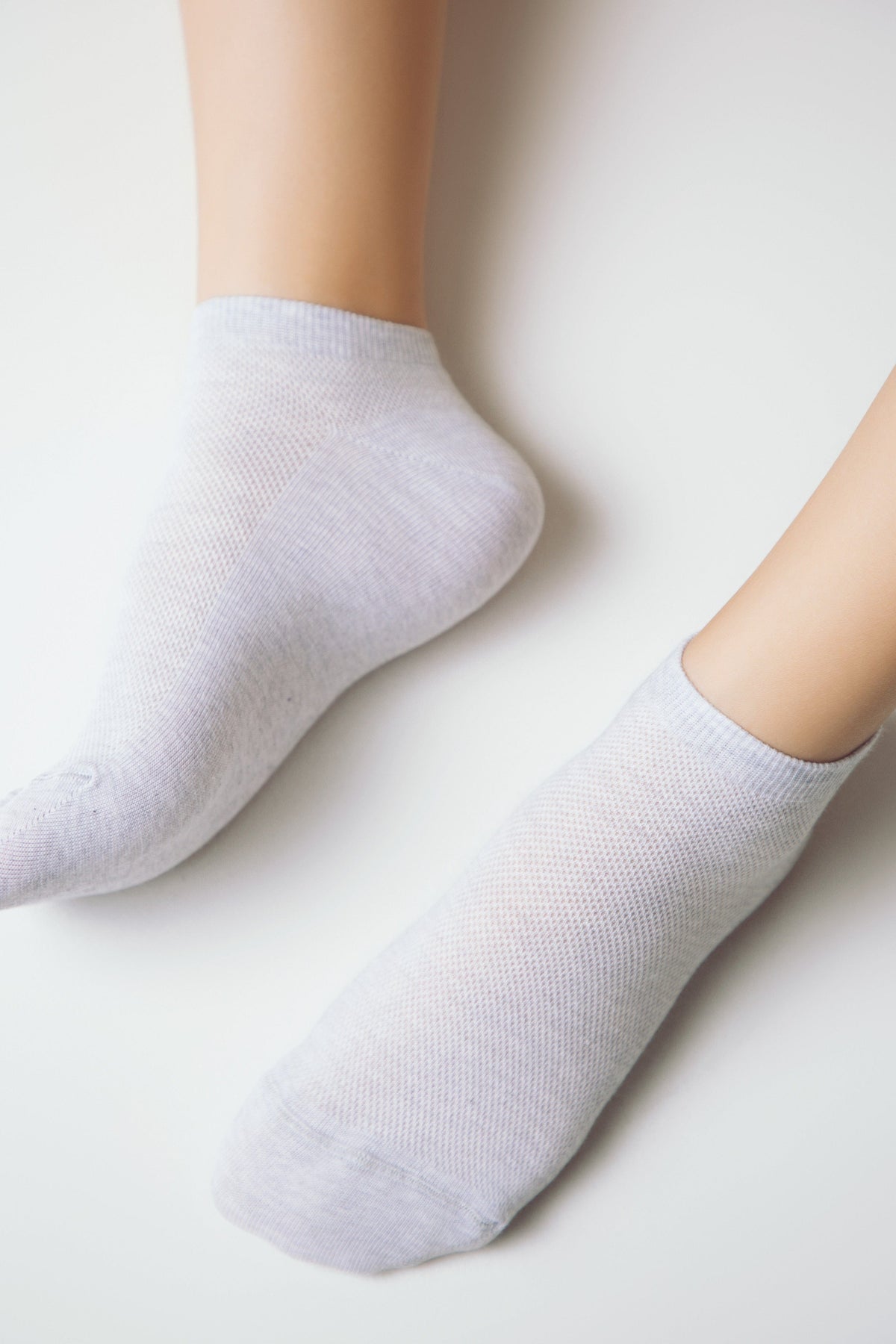 A pair of light gray ankle socks on human feet against a plain white background.