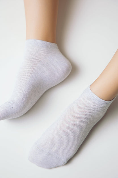 A pair of light gray ankle socks on human feet against a plain white background.