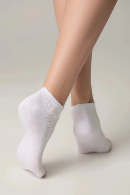 A pair of white ankle socks worn on the feet of a person against a plain, light grey background.