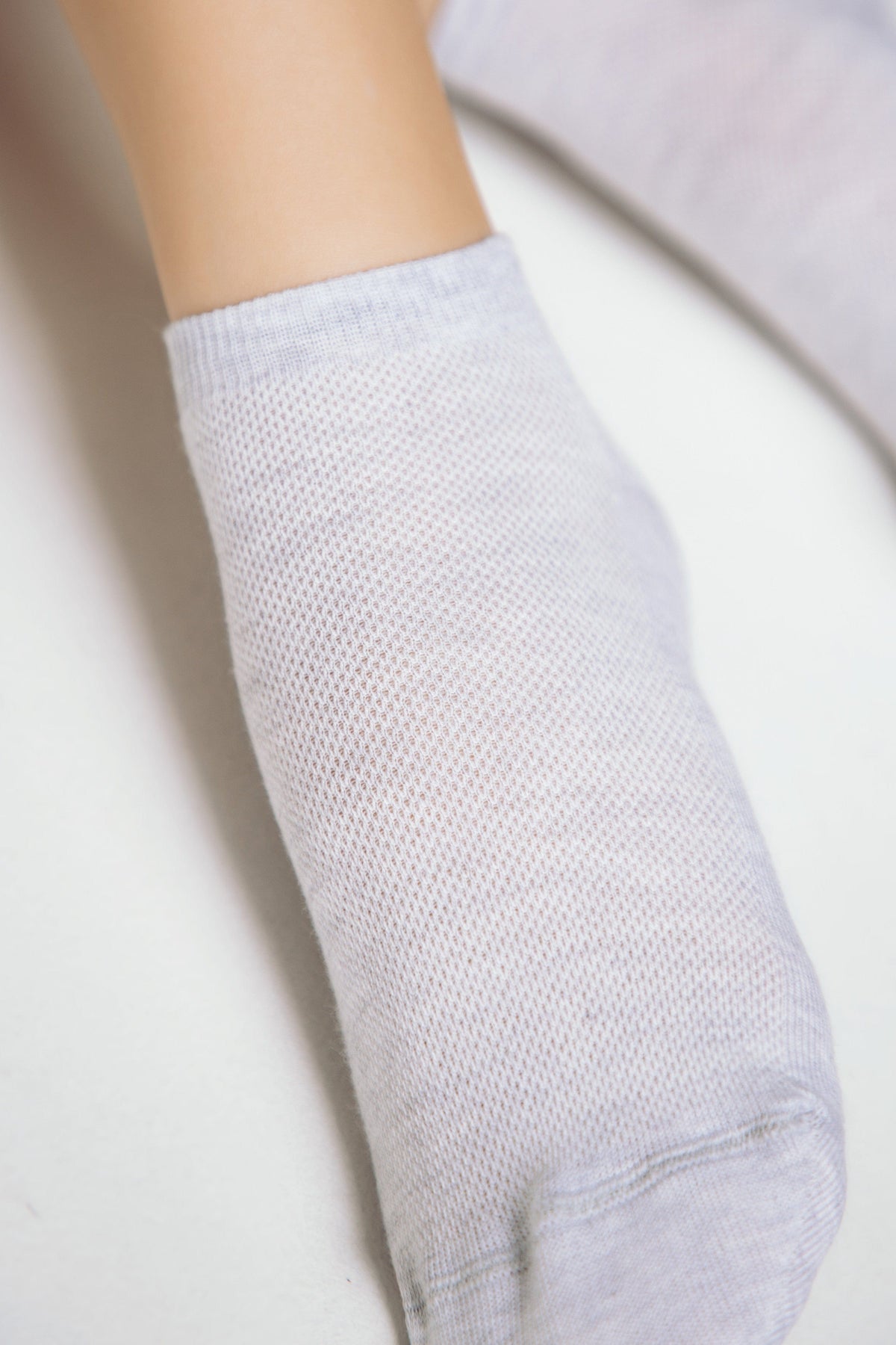 A light grey ankle sock made of a fine mesh fabric worn on a mannequin foot.