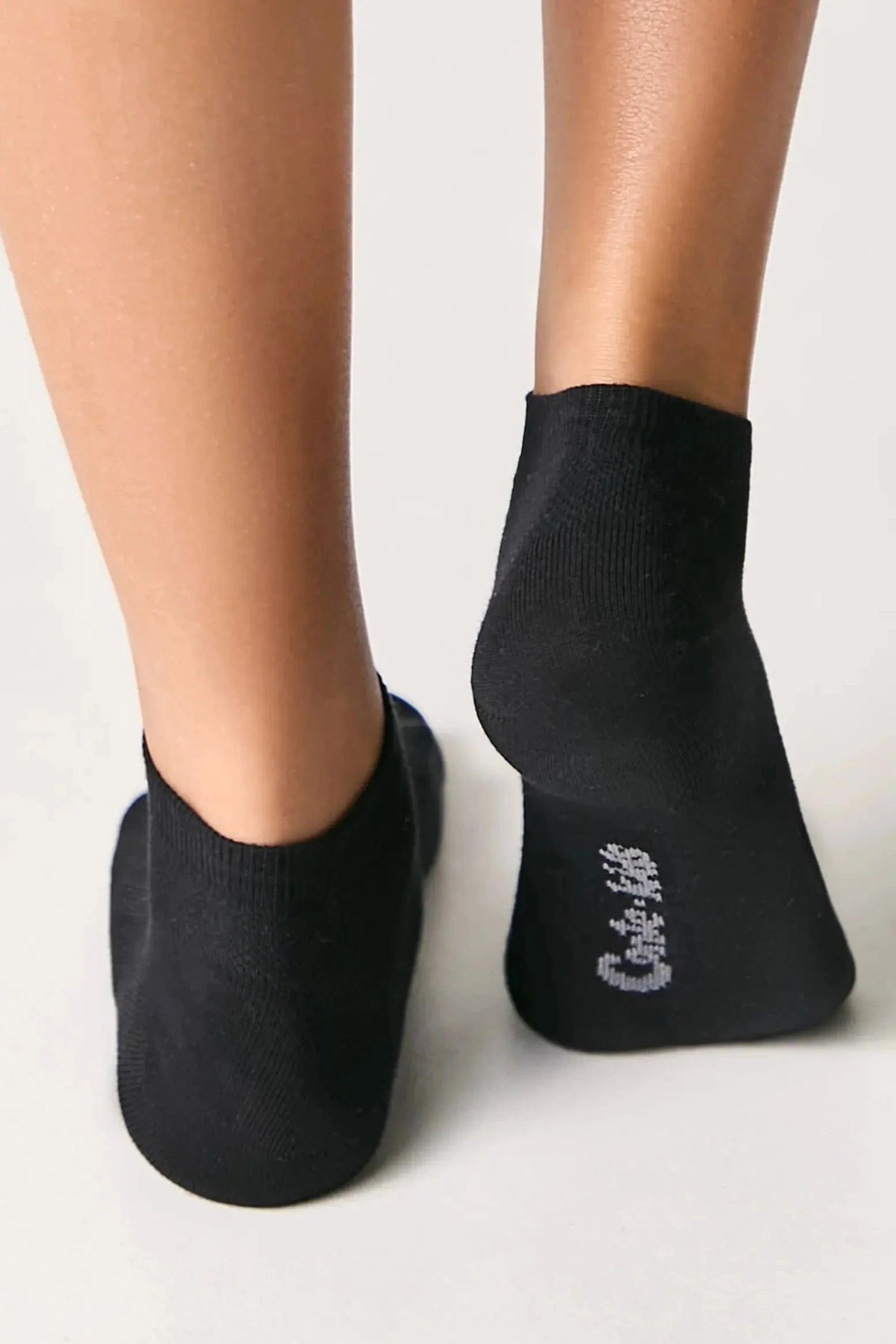 A pair of black ankle socks worn on the feet against a white background, with white branded text printed on the sole of the right sock.