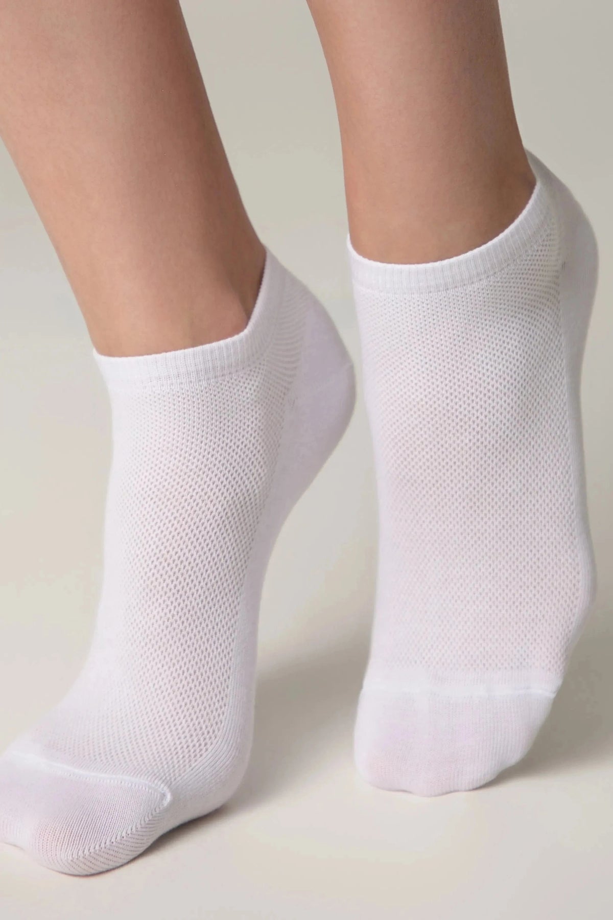 A pair of white ankle socks worn on feet against a solid light background.
