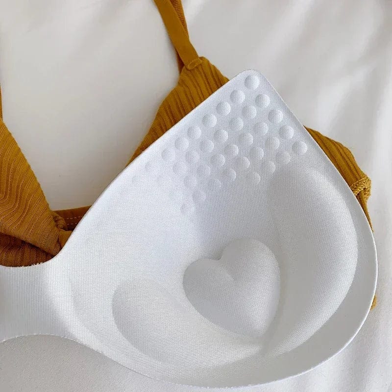 A white molded bra pad with a textured heart-shaped design and small raised circular bumps sits inside a mustard-yellow ribbed fabric bikini top.