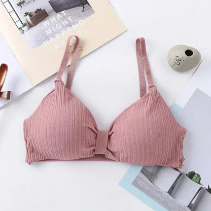 A mauve-colored ribbed bralette with thin shoulder straps and a simple center knot detail, displayed on a flat surface with decorative paper backgrounds.